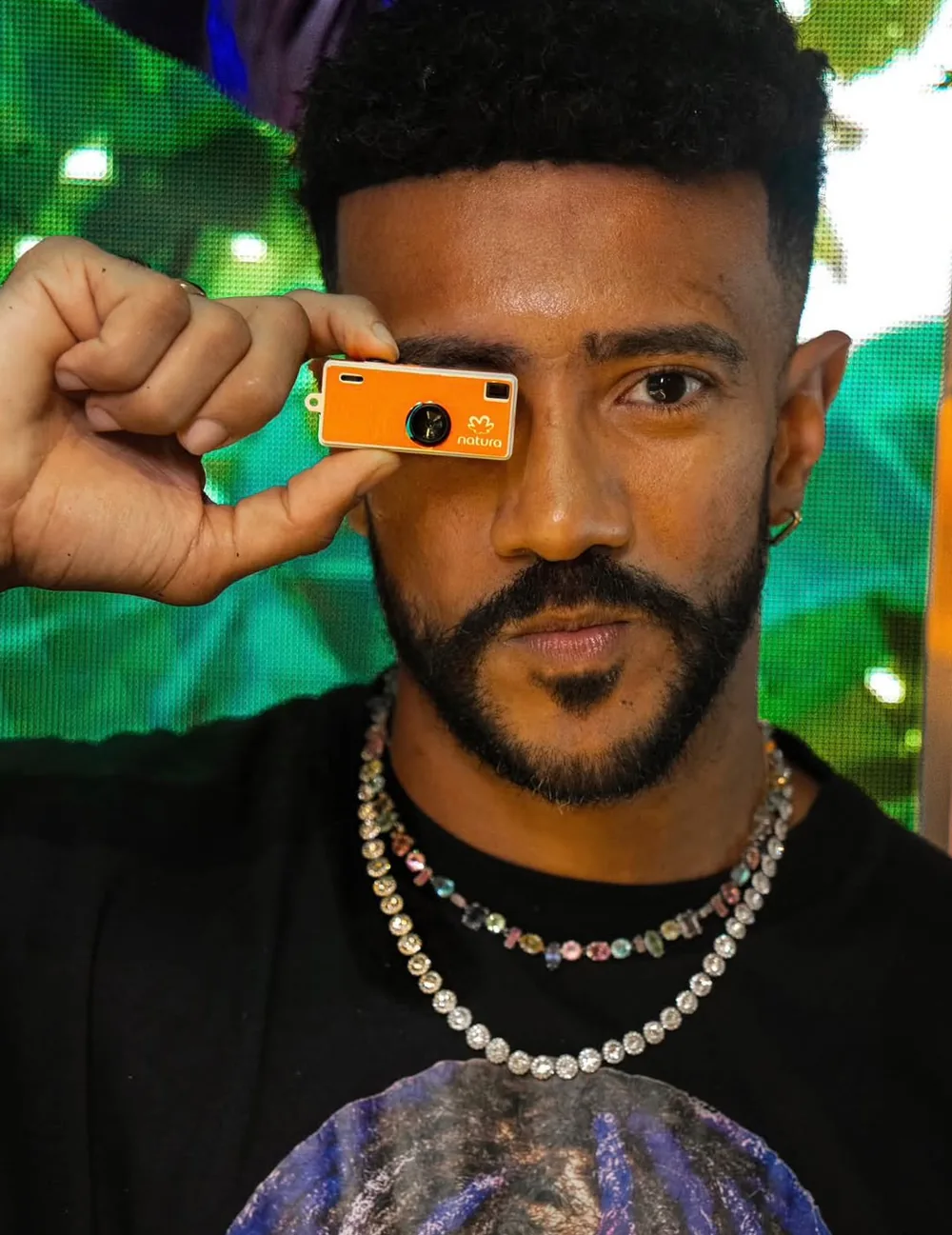 Influenciador segurando a câmera laranja da Natura na frente do olho
